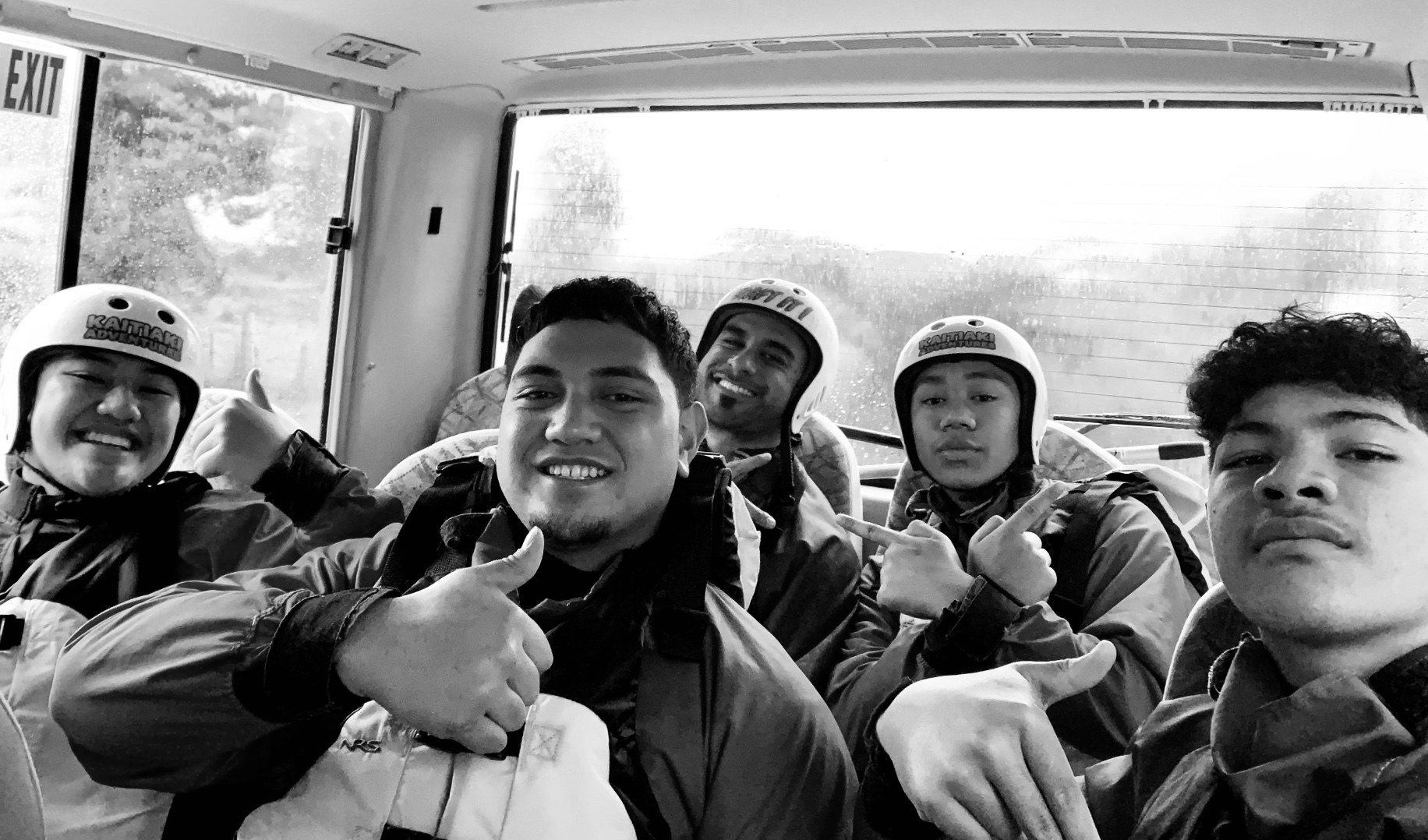 JAM students and mentors in rafting helmets, all smiles on the bus
