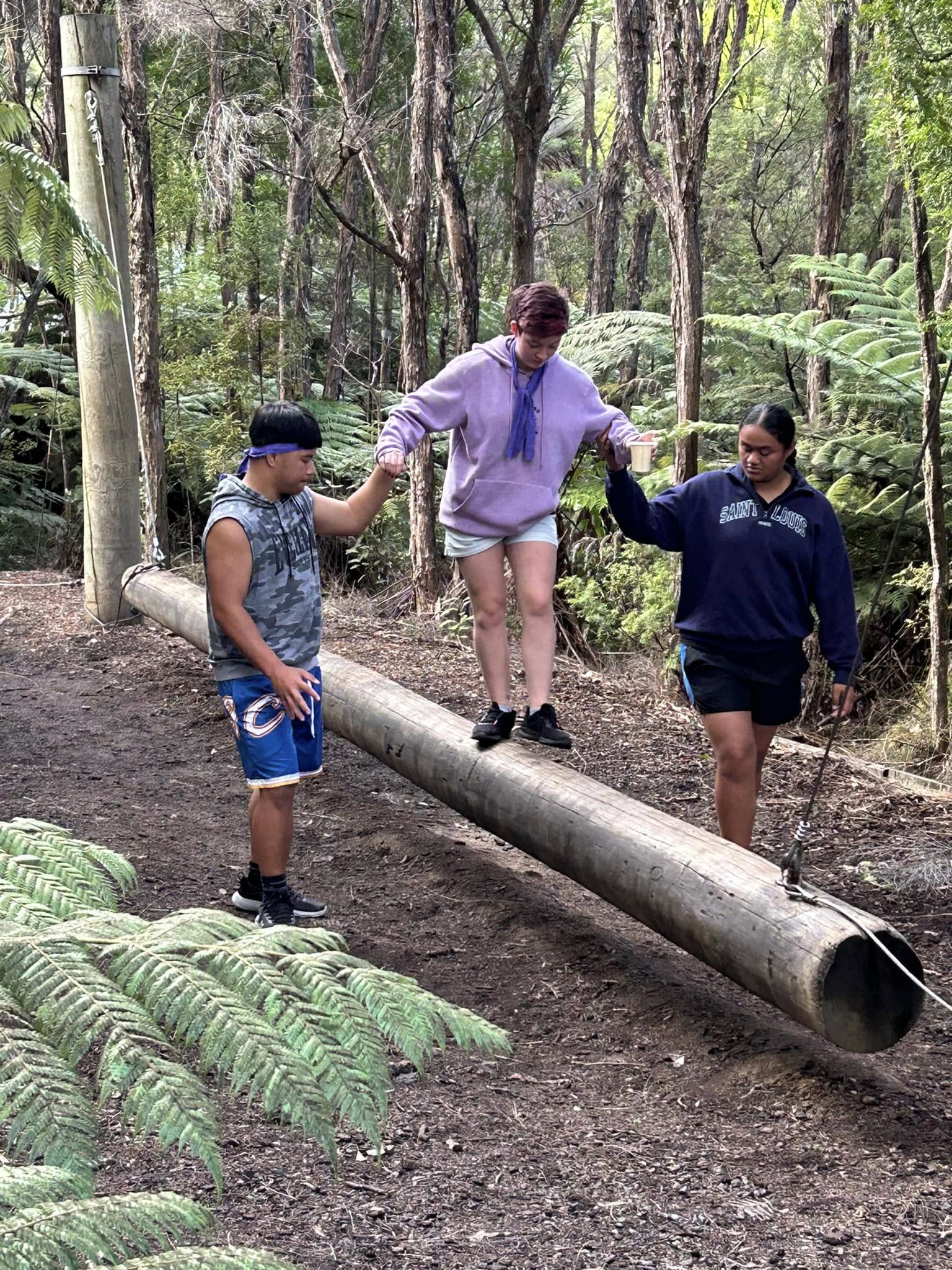 Students supporting a teammate balancing across the log walk on the bush confidence course